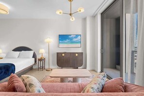 Ein Hotelzimmer mit Bett, Nachttischen, Schreibtisch, Sessel, Sofa, Deckenleuchte und Fenster.