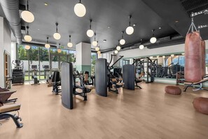 Ein Fitnessstudio mit Trainingsgeräten, großen Fenstern und hängenden Lampen.
