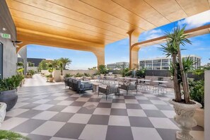 Eine Terrasse im Freien mit Schachbrettmuster-Bodenbelag, Sitzbereichen und Topfpflanzen.