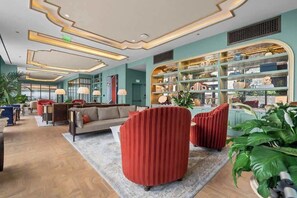 Eine moderne Hotelhalle mit einer Couch, roten Sesseln, einem Bücherregal und einer großen Pflanze.