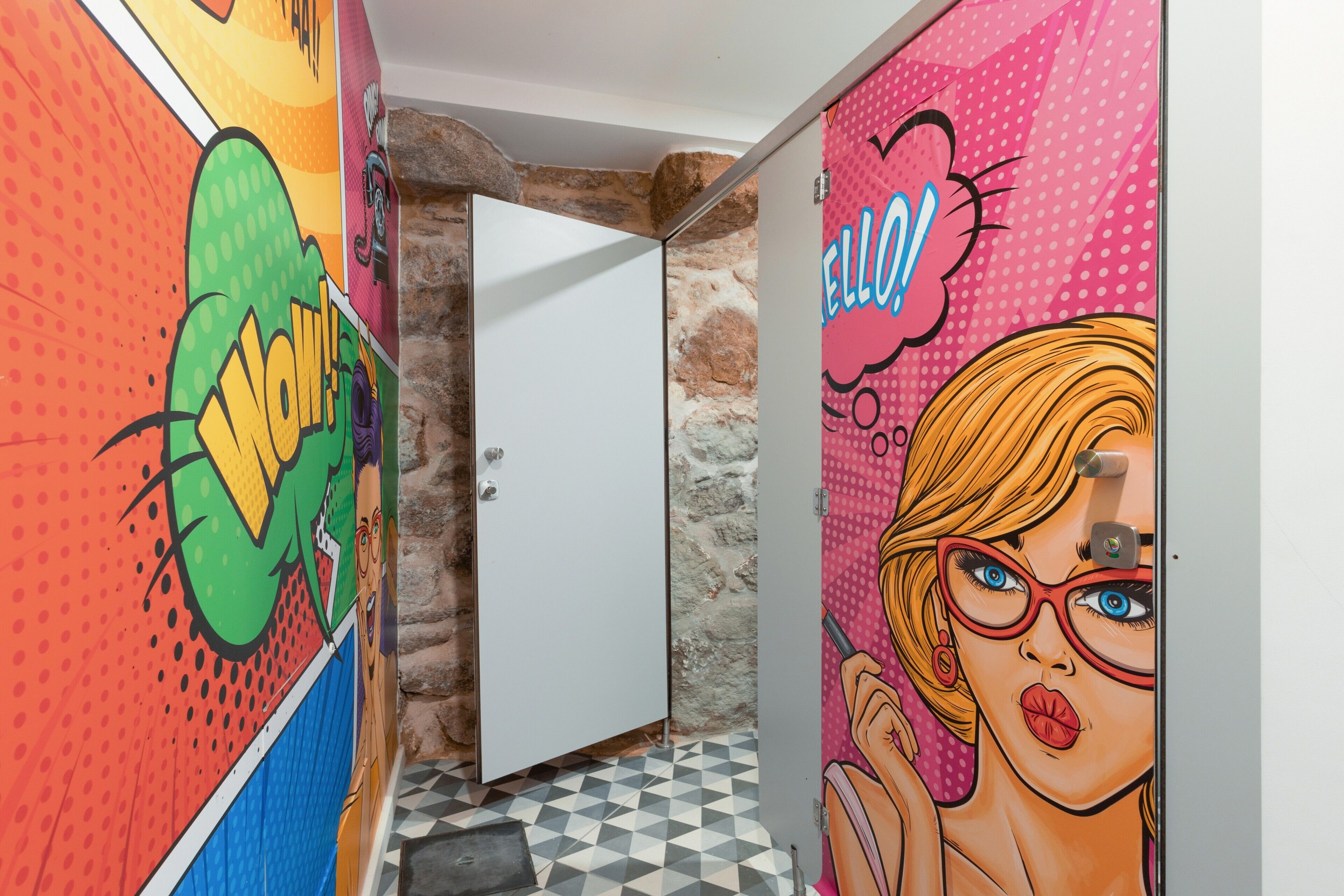 Un pasillo con murales de arte pop llamativos, una puerta blanca y un piso a cuadros.