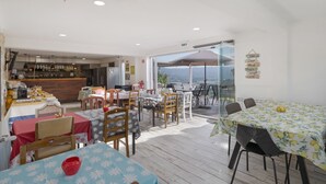 Angolo ristoro con tavoli e sedie, cucina sullo sfondo e vista attraverso una porta di vetro.