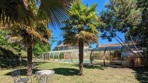 Un espacio al aire libre techado con piscina, rodeado de palmeras y una estructura de invernadero de vidrio.