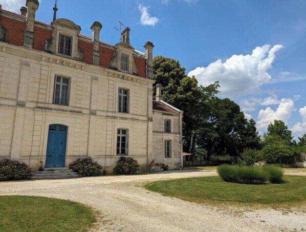 Un bâtiment à deux étages avec une porte bleue, une allée gravillonnée et une pelouse bien entretenue.