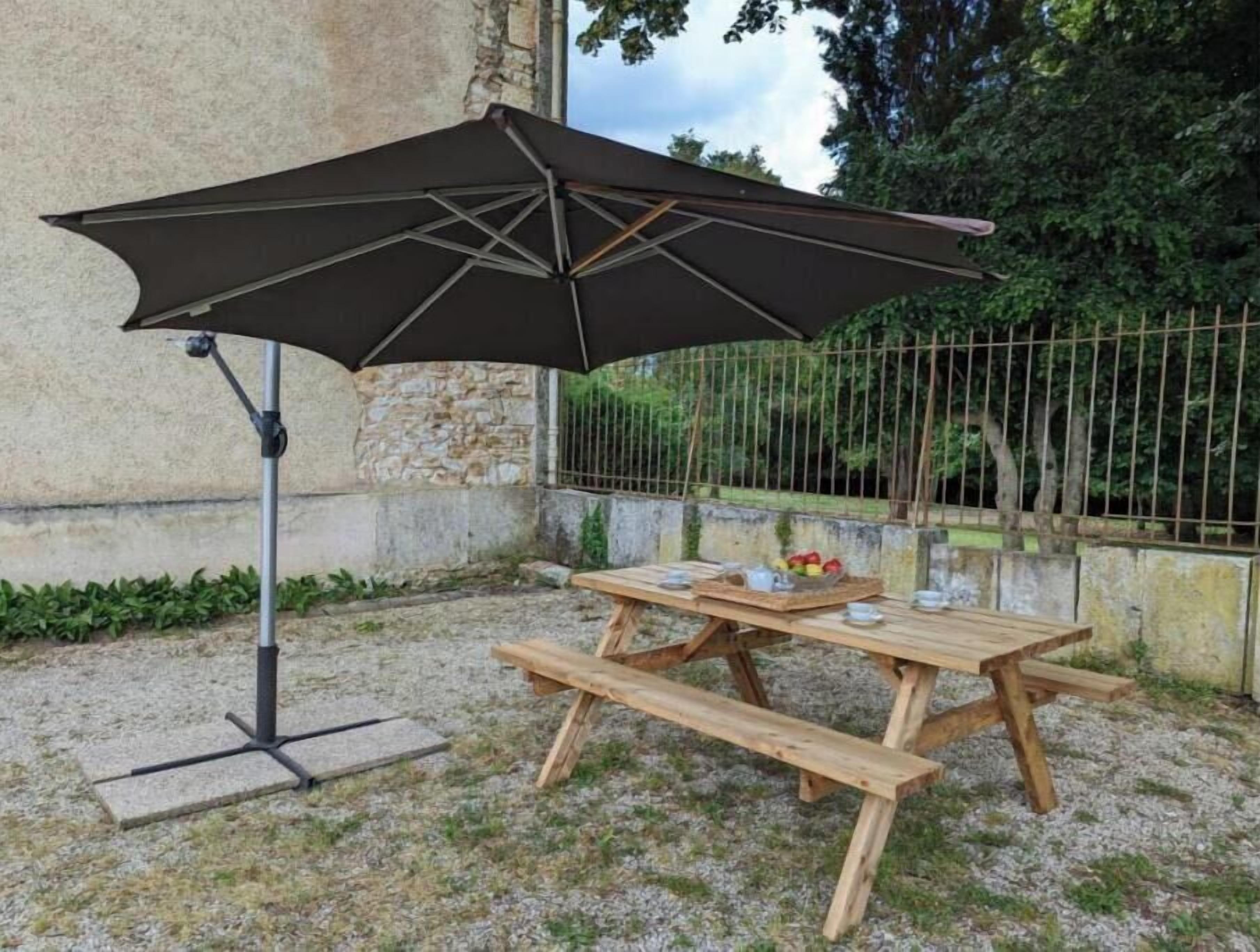 Une table de pique-nique avec un grand parasol, entourée de murs en pierre et d’une clôture en métal.