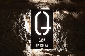 A sign with a large 'G' and the text 'CASA DA RUÍNA' against a textured wall.