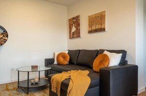 Ein modernes Wohnzimmer mit einem dunklen Sofa, zwei Zierkissen, einem Glastisch und einem kleinen Beistelltisch.