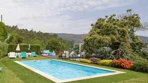 En rektangulär swimmingpool med ett omgivande däck, solstolar och utsikt över kullar i bakgrunden.