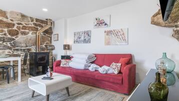 Un salón acogedor con un sofá rojo, una mesa de centro blanca, una pared de piedra y una chimenea.