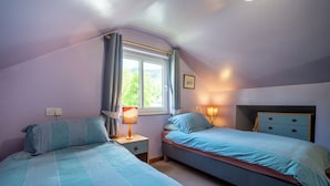 Quarto com duas camas, uma janela com cortinas, luminárias de cabeceira e um criado-mudo.