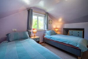 A bedroom with two beds, a window with curtains, bedside lamps, and a nightstand. - Oaks Lodge Cottage (Ambleside)