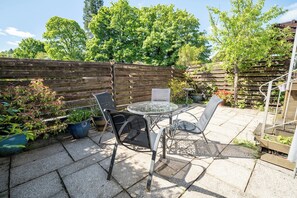 A patio with a round table and chairs, surrounded by a wooden fence and potted plants. - Oaks Lodge Cottage (Ambleside)