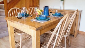 Mesa de jantar de madeira posta com pratos azuis, copos e jarra, rodeada por cadeiras de madeira.