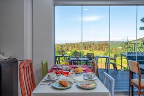 Un coin repas avec une table mise pour le petit-déjeuner, une vue sur la campagne et une grande fenêtre.