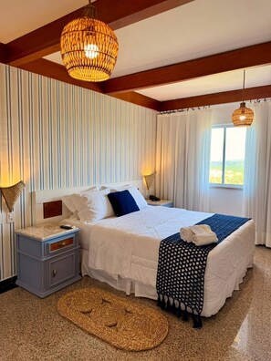 A bedroom with a bed, bedside tables, a woven rug, a hanging light fixture, and a window with curtains.