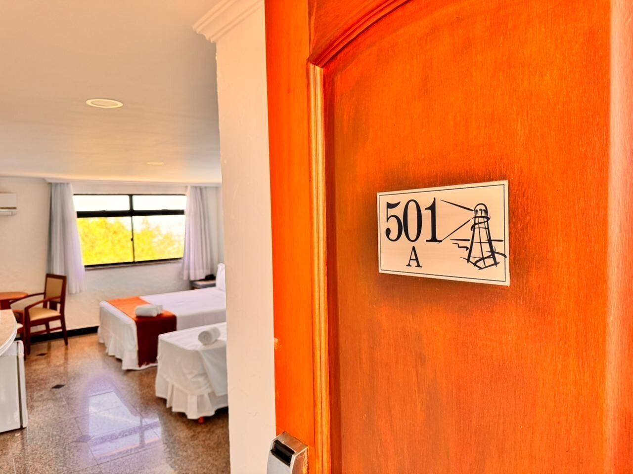Una habitación de hotel con cama, escritorio, silla y ventana con cortinas.