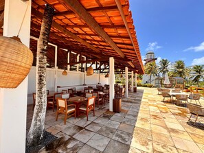 An outdoor patio with wooden tables and chairs, a tiled floor, and a covered area with a red roof. - Villa Nautilus by Be Happy (Fortaleza)