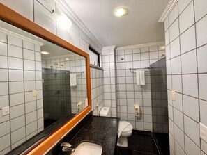 A bathroom with white tiled walls, a black countertop, a mirror, a toilet, and a shower. - Villa Nautilus by Be Happy (Fortaleza)