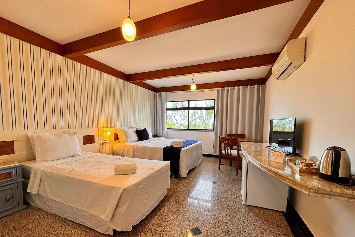 A hotel room with two beds, a desk, a chair, a television, and a coffee maker.