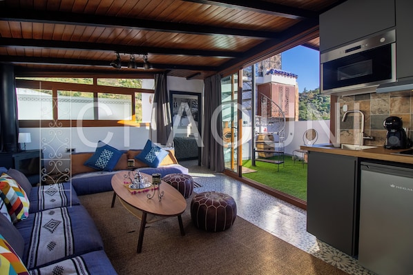 A modern living room with a sofa, ottomans, a coffee table, and a kitchen area with appliances. - Alojamientos Chaouni (Chefchaouen)