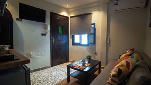 A compact living space with a kitchenette, a dark wooden door, a small table with a plant, and a sofa with colorful cushions.