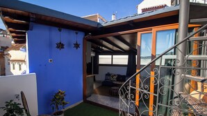 A residential balcony with a blue wall, a small garden area with artificial grass, and a metal railing.