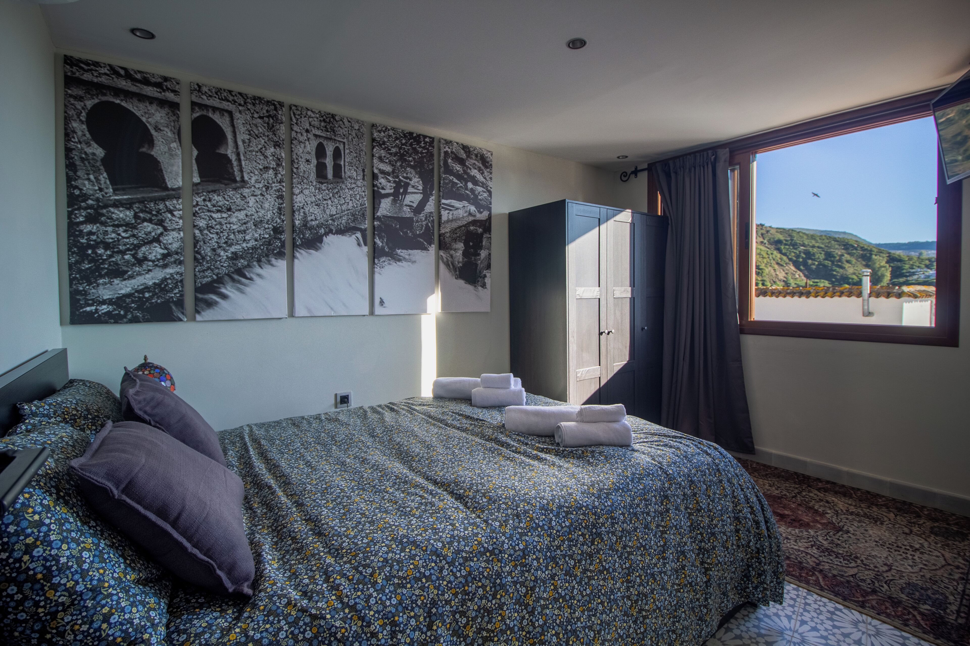 Een hotelkamer met een bed, een kledingkast, een raam met uitzicht en een wand met kunstwerk.