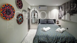 A bedroom with a bed, a mirror, a wall-mounted air conditioner, and a wall with a large circular design.