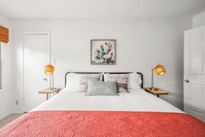 Ein Schlafzimmer mit einem Bett, zwei Nachttischlampen, einem gerahmten Kunstwerk an der Wand und einer Tür.