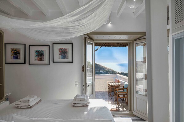 A bedroom with a bed, a balcony with a table and chairs, and framed pictures on the wall. - Villa Chora with sea and sunset view (Patmos)