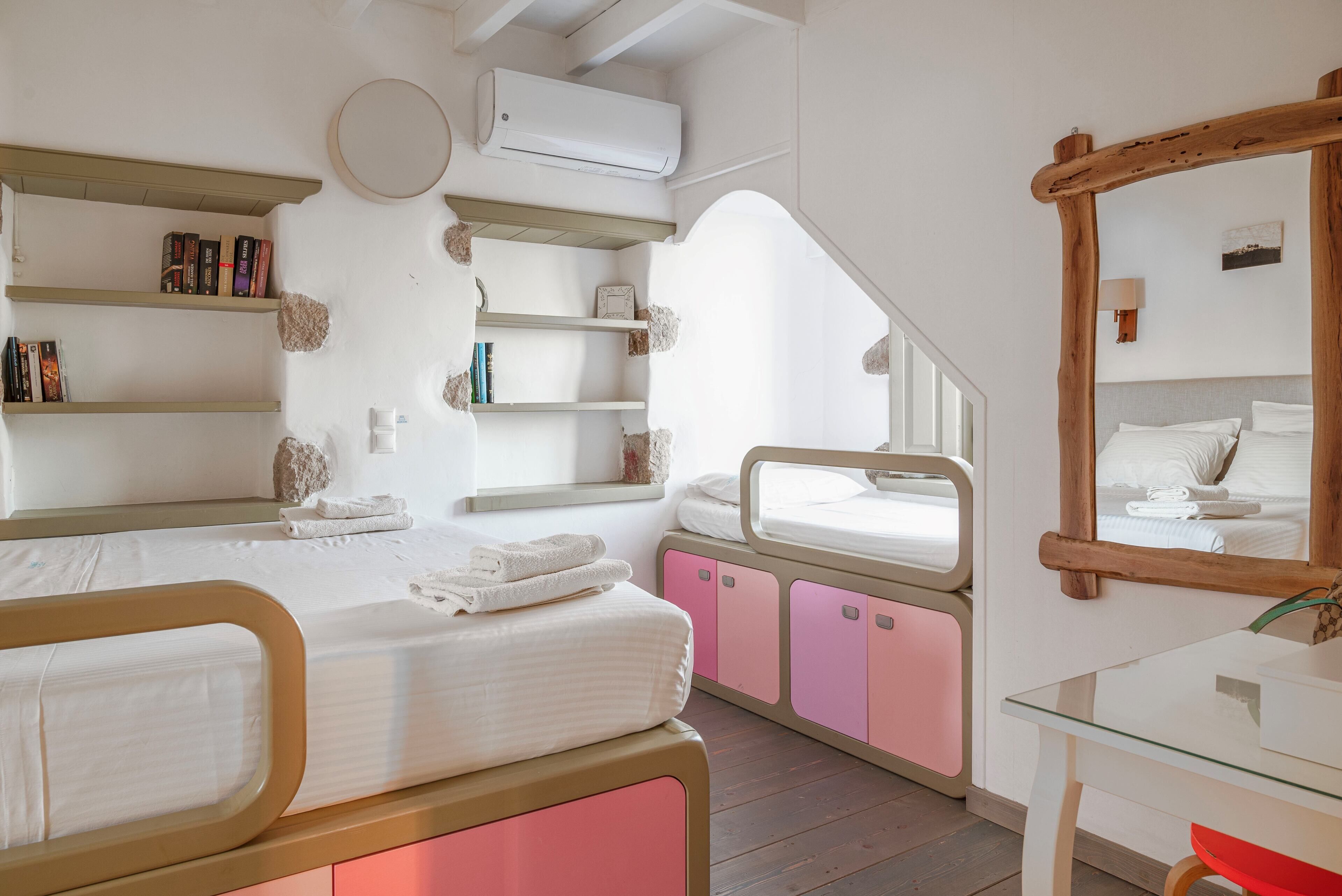 A bedroom with two beds, a desk, a mirror, and built-in shelves.