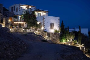 A multi-story building with stone walls, a staircase, and outdoor lighting. - Villa Chora with sea and sunset view (Patmos)