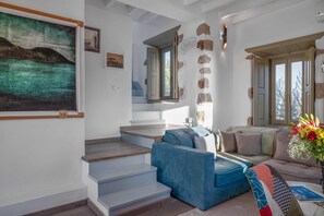 A staircase leading to a second floor, a blue sofa, a beige sofa, a painting, and a window with a view. - Villa Chora with sea and sunset view (Patmos)
