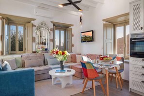 A living room with a sofa, a coffee table with a vase, a dining area with chairs, a TV, and a kitchen area with cabinets. - Villa Chora with sea and sunset view (Patmos)