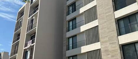 Un immeuble à plusieurs étages doté de balcons, d’un parking sécurisé et surplombant un ciel dégagé.