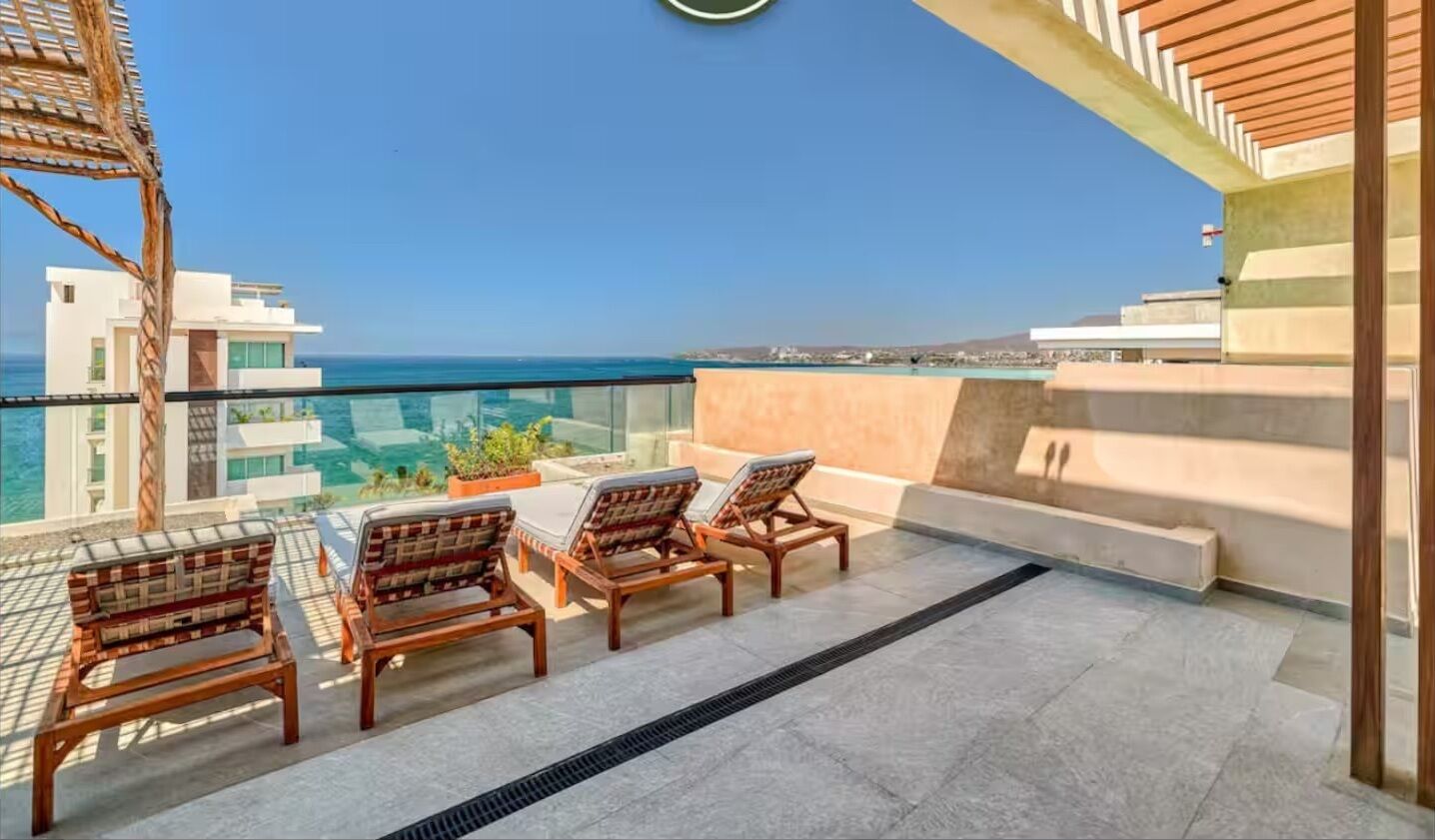 A balcony with a table and chairs, overlooking a coastal view.