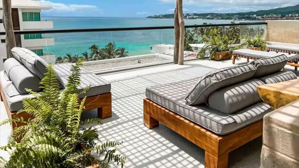 Uma varanda com vista para o oceano, uma pérgola de madeira e área de estar ao ar livre.