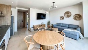 Um espaço de estar moderno com cozinha, área de refeições e sala de estar com sofá e televisão.