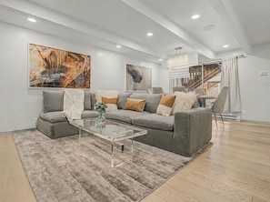 Ein modernes Wohnzimmer mit grauem Sofa, einem transparenten Glastisch und abstrakter Kunst an den Wänden.