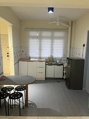 Eine kleine Küche mit Esstisch, Stühlen, einem Kühlschrank und einem Fenster mit Jalousien.