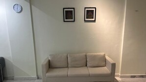A beige sofa against a wall with two framed pictures and a clock. - Homestay Ziyan with pool near beach (Port Dickson Town)