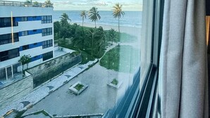 Uitzicht vanuit een raam op een gebouw met balkon, een geplaveid gebied en palmbomen.
