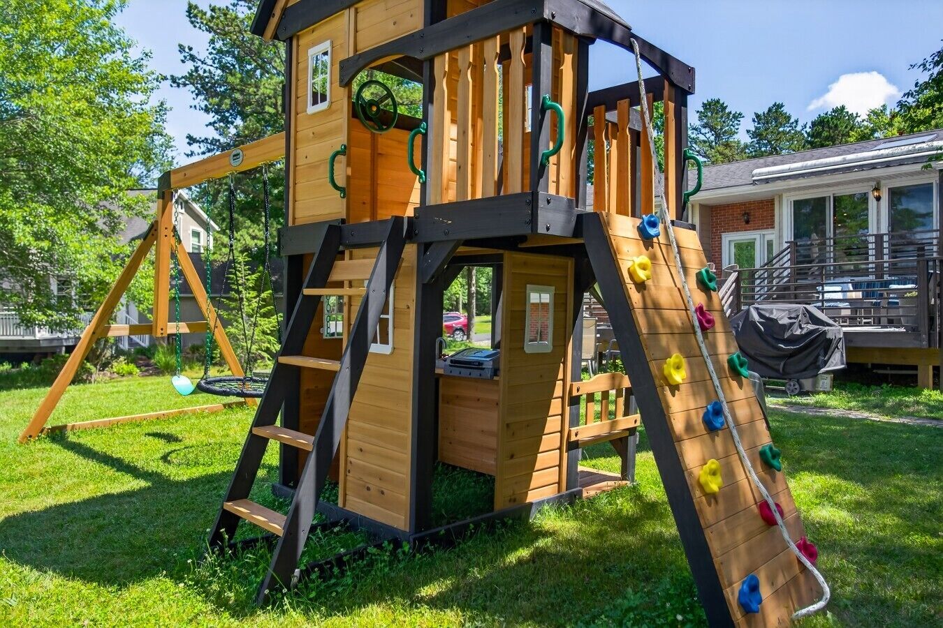 Een houten speelhuisje met een glijbaan, klimmuur en schommel.