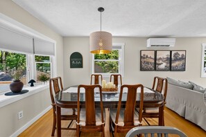 A dining area with a glass table, wooden chairs, a pendant light, and a view of greenery outside. - The Bear Creek Lake House: Lake-Front | Kayaks | Fire Pit | Grill | Beach (Jim Thorpe)