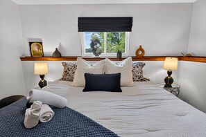A neatly made bed with a dark headboard, two bedside lamps, and a window with a view of trees. - The Bear Creek Lake House: Lake-Front | Kayaks | Fire Pit | Grill | Beach (Jim Thorpe)