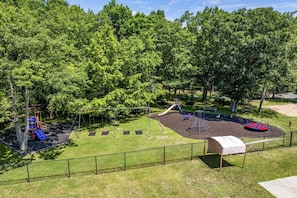 A playground with swings, slides, and climbing structures surrounded by trees. - The Bear Creek Lake House: Lake-Front | Kayaks | Fire Pit | Grill | Beach (Jim Thorpe)
