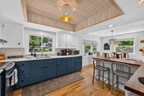 A modern kitchen with a central island, wooden ceiling, and large windows. - The Bear Creek Lake House: Lake-Front | Kayaks | Fire Pit | Grill | Beach (Jim Thorpe)