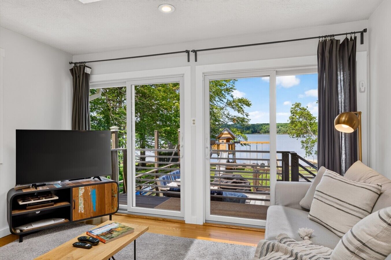 A living room with a television, sofa, and a view of a lake and outdoor area.