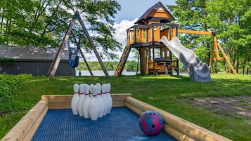 A backyard with a bowling alley, a wooden playhouse, and a slide.
