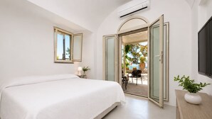 A bedroom with a bed, a bedside table, a lamp, a potted plant, and a sliding glass door leading to an outdoor area. - Villa Flaminia by My Villa Collection (Capri)